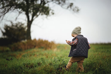 Rear view of boy standing on grassy field against sky - CAVF43508