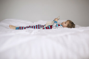 Seitenansicht eines Jungen, der sein Spielzeug hält, während er zu Hause auf dem Bett liegt - CAVF43509