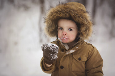 Porträt eines süßen Jungen, der auf einem Feld stehend Schnee isst - CAVF43515