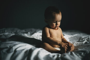 Shirtless Baby Mädchen sitzt auf dem Bett in der Dunkelkammer zu Hause - CAVF43521