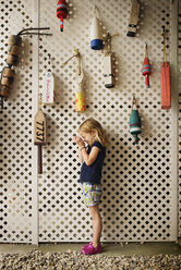Seitenansicht eines neugierigen Mädchens, das in seine schalenförmigen Hände schaut, während es neben Bojen steht, die an einer Trennwand hängen - CAVF43599