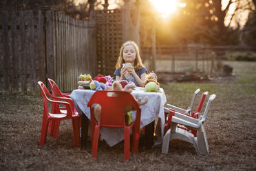 Porträt eines Mädchens, das bei Sonnenuntergang im Garten ein Sandwich isst - CAVF43621