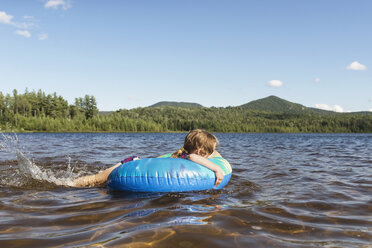 Side view of girl lying in inflatable ring on sea against blue sky - CAVF43625