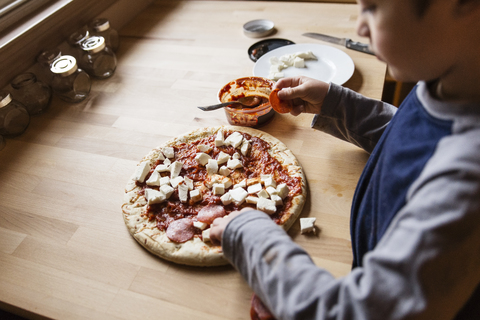 Hoher Blickwinkel auf einen Jungen, der zu Hause eine Pizza zubereitet, lizenzfreies Stockfoto
