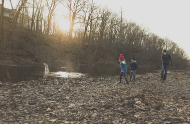 Playful family skimming stones in river at forest - CAVF43640