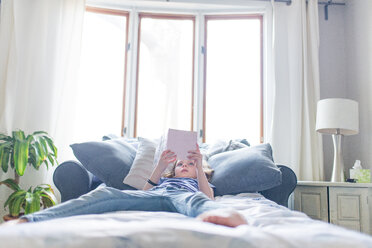 Mädchen liest ein Buch, während sie zu Hause auf dem Bett liegt - CAVF43645