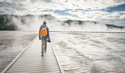Rückansicht eines Mannes, der auf der Promenade inmitten eines Sees gegen einen bewölkten Himmel läuft - CAVF43762