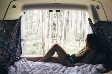 Woman looking through window while relaxing in camper van - CAVF43776