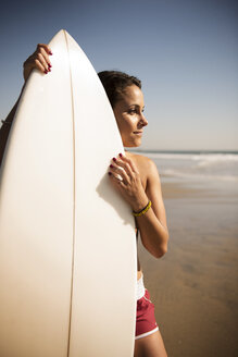 Nachdenkliche junge Frau steht mit Surfbrett am Strand - CAVF43783