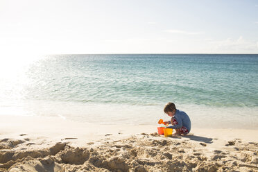 Junge spielt mit Sand am Strand gegen den Himmel an einem sonnigen Tag - CAVF43794