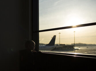 Boy looking through window while standing at airport - CAVF43799