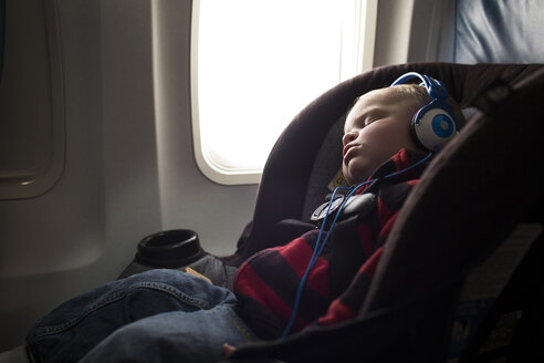 Junge mit Kopfhörern schläft im Flugzeug - CAVF43823