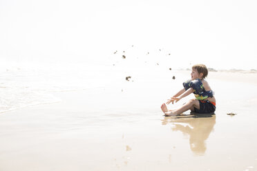 Seitenansicht des Jungen spielt mit Sand am Strand gegen den Himmel während des sonnigen Tages - CAVF43842