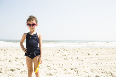 Portrait of girl in swimwear wearing sunglasses standing at beach during sunny day - CAVF43843