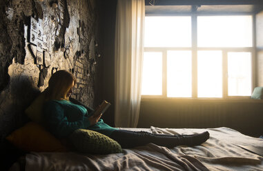 Teenager-Mädchen liest ein Buch, während sie zu Hause auf dem Bett liegt - CAVF43851