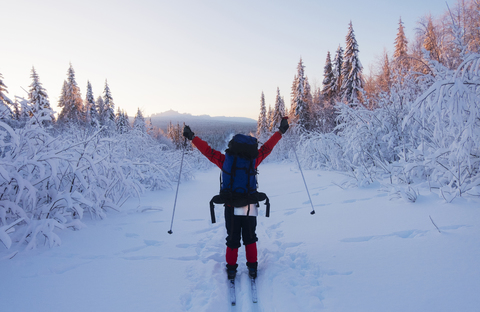 Rückansicht eines Wanderers mit erhobenen Armen auf einem schneebedeckten Feld bei klarem Himmel, lizenzfreies Stockfoto