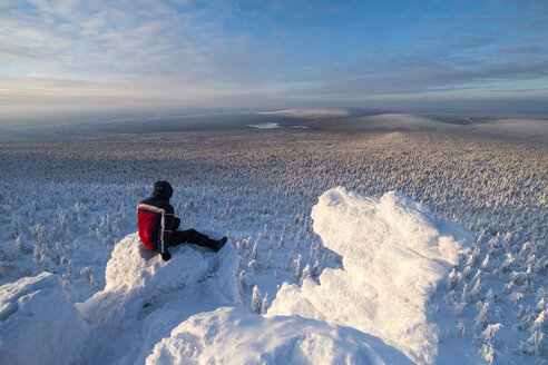 Wanderer, der die Aussicht betrachtet, während er auf einem schneebedeckten Berg gegen den Himmel sitzt - CAVF43859