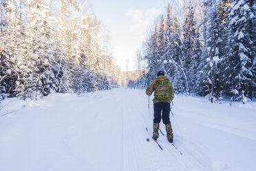 Rückansicht eines Mannes mit Rucksack beim Skifahren auf einem schneebedeckten Feld - CAVF43864