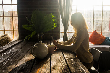 Woman using mobile phone by table at home - CAVF43870