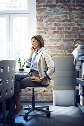 Businesswoman talking on phone while sitting on chair in office - CAVF43883