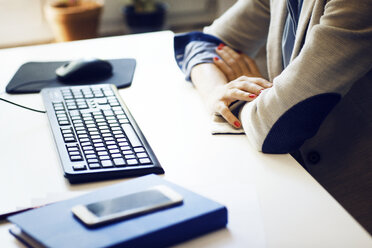 Mittelteil einer Geschäftsfrau mit verschränkten Armen, die am Schreibtisch im Büro sitzt - CAVF43887