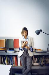 Geschäftsfrau, die einen Tablet-Computer benutzt und sich auf einen Tisch an der Wand im Büro stützt - CAVF43891