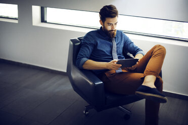 Geschäftsmann, der einen Tablet-Computer benutzt, während er auf einem Stuhl im Büro sitzt - CAVF43895