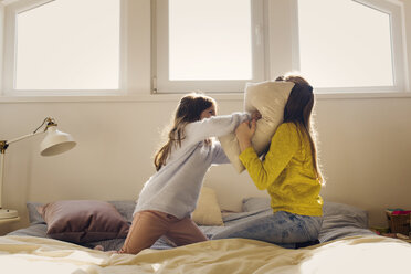 Sisters fighting with pillows on bed at home - CAVF43936