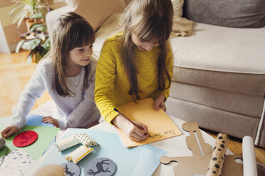 Lächelndes Mädchen neben seiner Schwester, die am Tisch auf Papier schreibt - CAVF43939