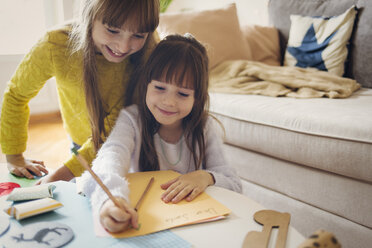 Sister by girl writing on paper at home - CAVF43940