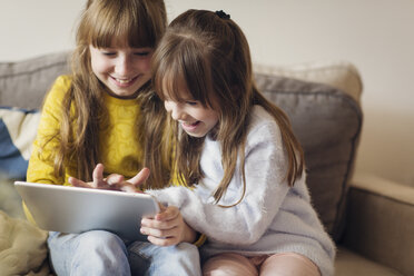 Schwestern, die zu Hause sitzend in einen Tablet-Computer schauen - CAVF43948