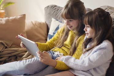 Sisters using tablet computer while sitting on sofa at home - CAVF43949