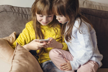 Sisters using phone on sofa at home - CAVF43953