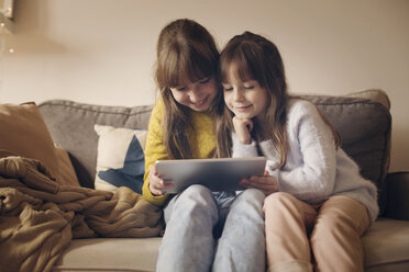 Schwestern, die zu Hause sitzend in einen Tablet-Computer schauen - CAVF43968