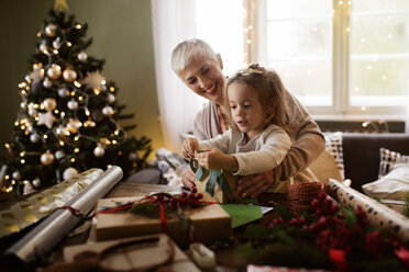 Mädchen und Großmutter packen zu Weihnachten Geschenke am Tisch ein - CAVF43969
