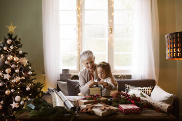 Großmutter hilft einem Mädchen beim Verpacken von Weihnachtsgeschenken - CAVF43970