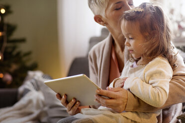 Großmutter küsst Enkelin und hält Tablet-Computer zu Hause - CAVF43986
