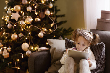 Mädchen mit Tablet-Computer auf dem Sofa sitzend während der Weihnachtszeit - CAVF43989