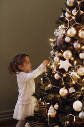 Mädchen schmückt Weihnachtsbaum zu Hause - CAVF43990