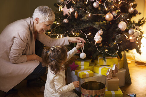 Großmutter hilft der Enkelin beim Schmücken des Weihnachtsbaums zu Hause - CAVF43991