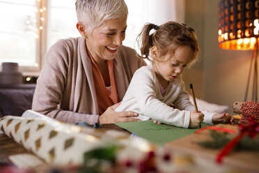 Happy grandmother assisting granddaughter in drawing at home - CAVF43996