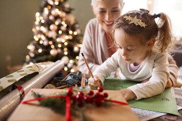 Großmutter betrachtet Enkelin beim Zeichnen auf Papier während Weihnachten - CAVF43997