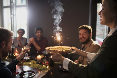 Frau serviert Freunden zu Weihnachten Torte mit brennenden Kerzen - CAVF44015