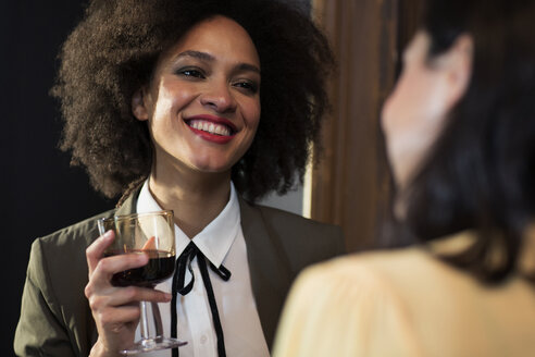 Lächelnde Frau im Gespräch mit einem Freund bei einem Glas Wein zu Hause - CAVF44026