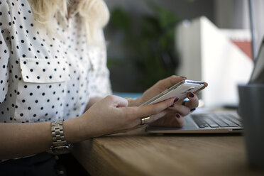 Mittelteil einer Frau, die ein Smartphone am Tisch benutzt - CAVF44040