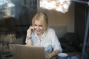 Happy woman using laptop at home office - CAVF44049
