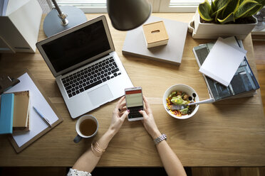 Overhead view of woman using smart phone at desk in home office - CAVF44053