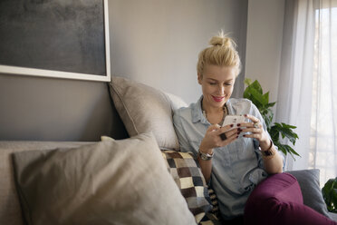 Glückliche Frau, die ein Smartphone benutzt, während sie zu Hause auf dem Sofa sitzt - CAVF44066