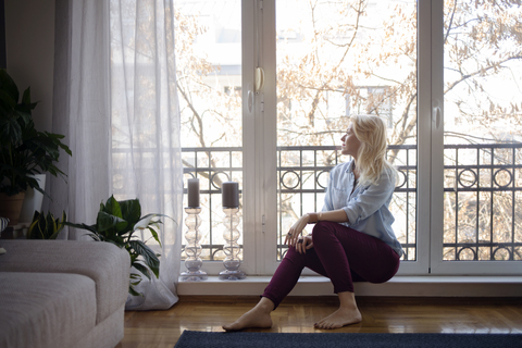 Nachdenkliche Frau schaut durch das Fenster zu Hause, lizenzfreies Stockfoto