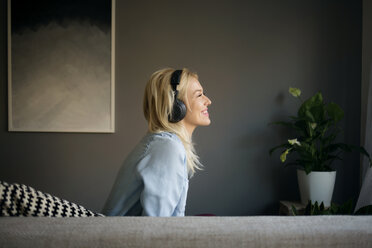Seitenansicht einer glücklichen Frau, die zu Hause auf dem Sofa sitzt und Musik hört - CAVF44070